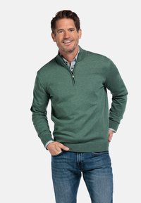 Groene gebreide pullover met een kwart-rits kraag, geribde manchetten en zoom. Gedragen over een gestreept overhemd met kraag, gecombineerd met blauwe spijkerbroek.