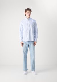 Chemise boutonnée rayée bleu clair, col, manches longues, associée à un jean bleu clair et des baskets blanches. Design minimaliste et palette de couleurs.
