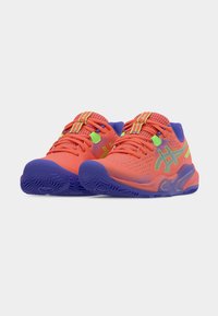 Φωτεινά πορτοκαλί αθλητικά παπούτσια με επάνω μέρος από δίχτυ, μοβ σόλα, πράσινες και κίτρινες λεπτομέρειες, και ασφαλές σύστημα κορδονιών.