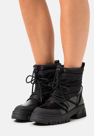 Černé zateplené boty s polstrovaným svrškem, kulatou špičkou, strukturovaným materiálem a silnou gumovou podrážkou. Mají tkaničky a boční dekorační prvky.
