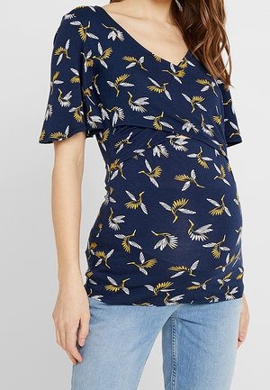 Zwangerschapstop in marineblauwe stof met een bloemmotief in geel en wit. Voorzien van een V-hals, korte mouwen en plooien aan de zijkanten.