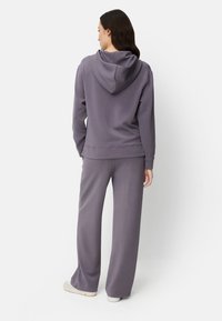 Lilla hættetrøje med en forreste kængurulomme og snøre i hætten, kombineret med matchende bukser med vide ben. Blødt stof med minimal tekstur.