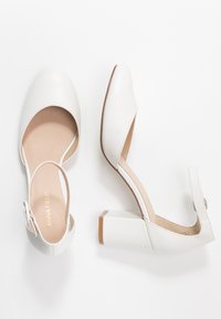 Weiße Lederhighheels mit einem Riemen, offener Zehenpartie und quadratischem Blockabsatz. Das Innere ist beige mit einer geprägten Markenbezeichnung.