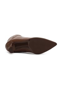 Bottine en cuir marron avec un bout pointu et une silhouette épurée. Présente une texture lisse et un talon robuste légèrement courbé.