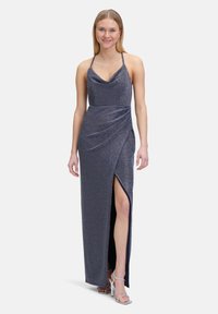 Schimmerndes navyblaues Kleid mit einem Cowl-Ausschnitt, dünnen Tr�ägern und einem Oberschenkel-spitzen Schlitz. Der drapierte Schnitt betont die Silhouette. Kombiniert mit silbernen High Heels.
