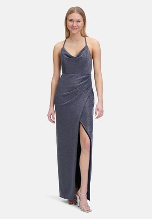 Schimmerndes navyblaues Kleid mit einem Cowl-Ausschnitt, dünnen Trägern und einem Oberschenkel-spitzen Schlitz. Der drapierte Schnitt betont die Silhouette. Kombiniert mit silbernen High Heels.