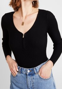 Body à manches longues côtelé noir avec un décolleté en V profond et une fermeture éclair à l'avant. Associé à un short en denim bleu clair taille haute.