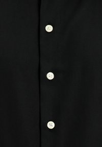 Czarna koszula o gładkiej fakturze z pięcioma białymi guzikami z przodu, podkreślająca klasyczny fason zapinany na guziki.