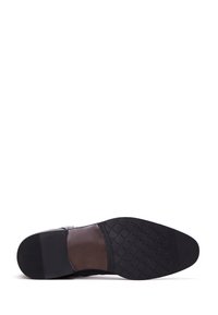 Suela de zapato de cuero negro con goma texturizada para agarre. Presenta una parte superior de cuero suave con un sutil diseño tejido y forma curvada.