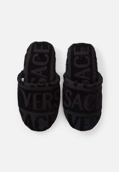 Μαύρες πλεκτές παντόφλες με ανάγλυφο λογότυπο. Ο σχεδιασμός είναι ανοιχτός στη μύτη με στρογγυλή μορφή και μαλακή υφή για άνεση.