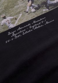 Sort T-shirt med en vintage fodboldgrafik på forsiden. Tekst under billedet i hvid skrift angiver en kampdato og score.