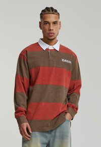 Langermet rugbyshirt med røde og brune horisontale striper, hvit krage og et logo på venstre bryst.