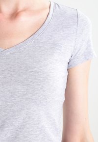 T-shirt grigia a maniche corte con scollatura a V. Tessuto leggero e morbido, con un piccolo logo stampato vicino al collo.