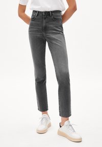 Jean droit taille haute en denim gris foncé avec des accents délavés, associé à des baskets blanches avec une semelle texturée et des lacets.