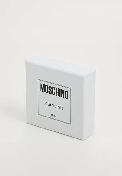 Λευκό ορθογώνιο κουτί Moschino Couture Milano με μαύρο κείμενο στο κέντρο, σε λευκό φόντο, γωνιακά για να φαίνεται το μπροστινό και το πλάι.