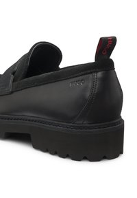 Scarpa slip-on in pelle nera con dettagli in suede, suola spessa in gomma e finitura texturizzata. Presenta un pratico tirante brandizzato e logo in rilievo.