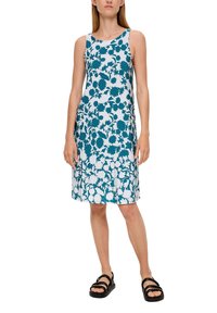 Ärmelloses Kleid in Weiß mit türkisfarbenem Blumenmuster, A-Linie-Silhouette, knielang. Kombiniert mit schwarzern Sandalen, glatte Stoffoberfläche.