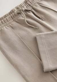 Pantalons de jogging beiges en tissu texturé avec une taille élastique et un cordon de serrage. Comprend une poche latérale et des coutures plates.