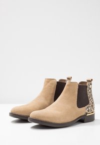 Stivaletti in suede beige con pannelli laterali elastici, dettaglio in stampa leopardata e tacco in legno basso. Cuciture decorative lungo la suola.