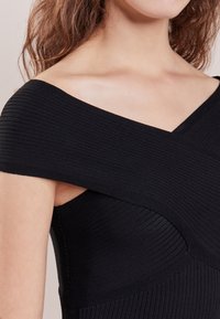 Czarna, prążkowana sukienka z asymetrycznym fasonem na jedno ramię, z teksturowanej tkaniny i dopasowanym kroju. Podkreśla dekolt i ramię.