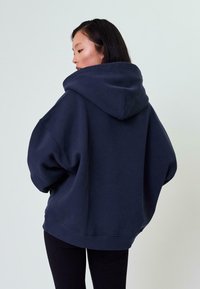 Felpa oversize blu navy realizzata in morbido tessuto, con un ampio cappuccio, spalle dropped e polsini a coste all'orlo e alle maniche.