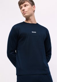 Camisa de manga larga azul marino con cuello redondo, que presenta un logo blanco de "BOSS" en el pecho y una textura suave y lisa.