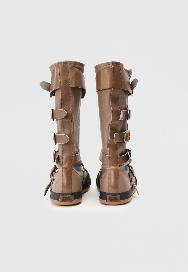 Tall brown leather boots with adjustable straps, textured panels, and a flat sole. Notable hardware includes buckles and a sleek design.