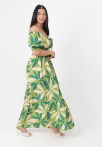 Grön maxi-klänning med off-shoulder ärmar, prydd med ett stort bladmönster i mörkgrönt och krämfärgat. Flödande tyg med en smal midja.