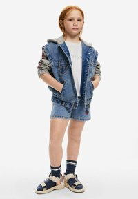 Džínová vesta s šedou kapucí, bílým tričkem, džínovými šortkami s květinovým motivem a pestrobarevnými sandály se pásky.