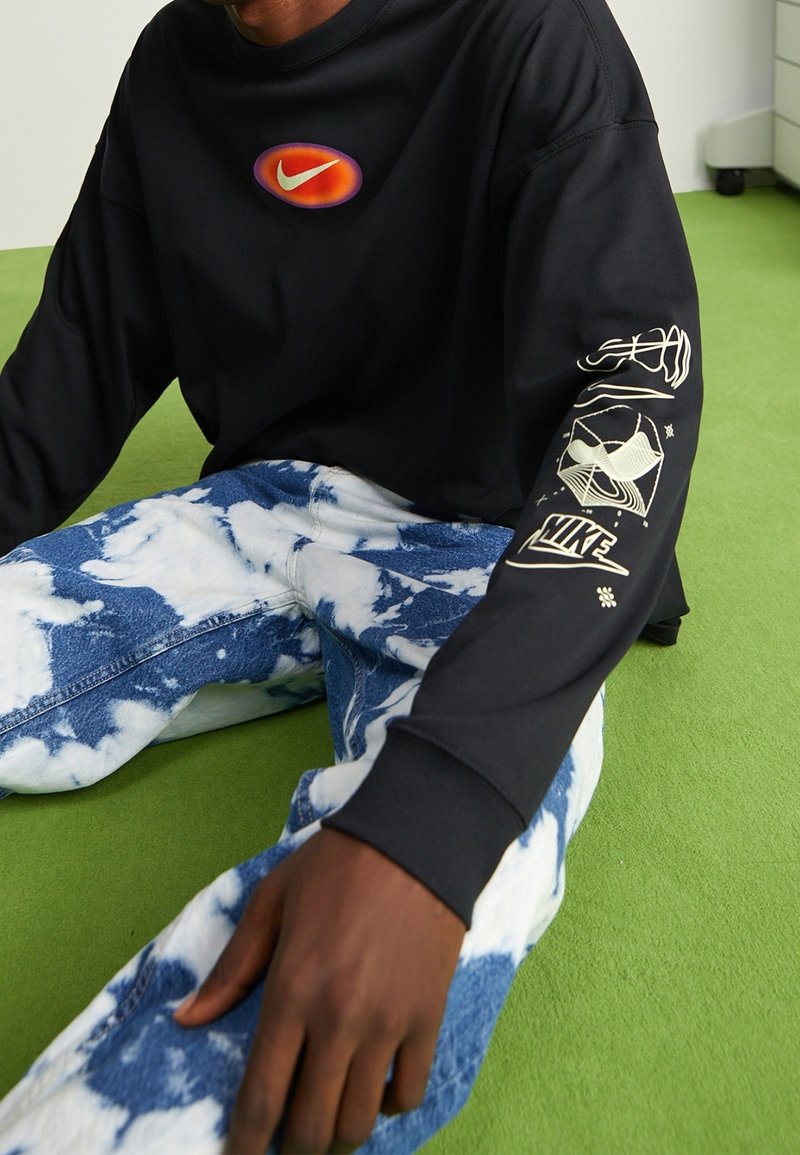 Musta pitkähiha barco, jossa on monivärinen Nike-logo; siniset ja valkoiset solumuovifarkut; teksturoitu kangas; istuu vihreällä pinnalla.