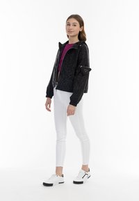 Giacca nera con zip, motivo testurizzato, cappuccio e polsini elasticizzati; abbinata a una maglietta viola, pantaloni bianchi e sneakers in bianco e nero.