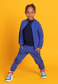 Niebieski dres z kurtką bomber zapinaną na zamek i elastycznymi ściągaczami, połączony z kolorowymi trampkami typu high-top z wielobarwnymi akcentami i wzorami.