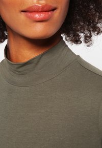 Haut à col montant vert olive en tissu doux et extensible. Coupe près du corps avec une texture côtelée subtile et un col lisse.