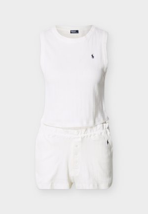 Λευκό ριμπ τοπ χωρίς μανίκια σε κομμένο μήκος και αντίστοιχα ριμπ σορτς με ελαστική μέση, διακοσμημένα με μικρά σκοτεινά κεντημένα λογότυπα.