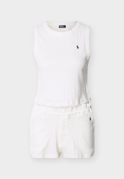 Λευκό ριμπ τοπ χωρίς μανίκια σε κομμένο μήκος και αντίστοιχα ριμπ σορτς με ελαστική μέση, διακοσμημένα με μικρά σκοτεινά κεντημένα λογότυπα.