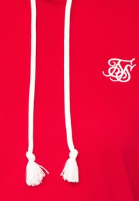 Felpa rossa con cappuccio e lacci bianchi con pon pon. Include un piccolo logo ricamato bianco nella zona del petto. Comodo materiale in cotone.