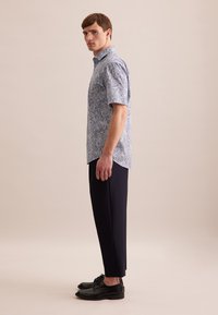 Koszula z krótkim rękawem w niebieski wzór paisley, z kołnierzykiem. Połączona z eleganckimi, czarnymi butami do garnituru i dopasowanymi ciemnymi spodniami.