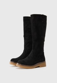 Bottes noires en daim montantes avec une finition texturée, fermeture éclair sur le côté et semelle en caoutchouc marron contrastante. Présente un accent piqué autour de la base.