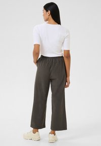 Pilkos plačios kelnės su elastine juosmens juosta, derinamos su aptemptu baltu marškinėliu ir kreminiais sportbačiais. Lygios audinio tekstūros.