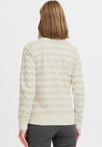 Sweat-shirt beige clair avec un motif zigzag texturé et des poignets et un ourlet côtelés. Tissu doux avec une coupe décontractée et un col rond. Vue arrière.