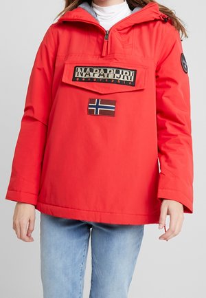 Persona que lleva una chaqueta roja Napapijri con un bolsillo frontal y un parche con la bandera de Noruega, combinada con vaqueros azul claro.