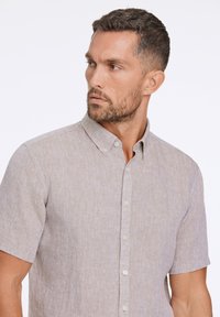 Camicia a maniche corte con colletto in lino beige chiaro, con un motivo tessuto testurizzato e chiusura con bottoni, caratterizzata da piccoli bottoni bianchi.