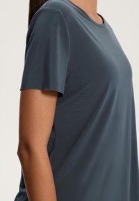 Sötétszürke, rövid ujjú sportpóló sima textúrával, kerek nyakkivágással és diszkrét perforált részletekkel az oldalon.