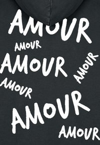 Črna kapuca z ponavljajočim se belim napisom "AMOUR" v različnih velikostih in orientacijah, z mehko teksturo blaga.