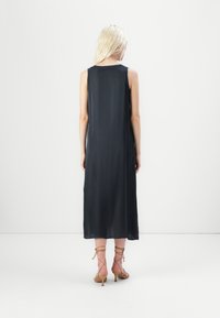 Rochie neagră fără mâneci cu o siluetă fluidă, realizată dintr-un material ușor. Asortată cu sandale cu toc înalt, cu bretele, de culoare bej.