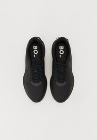 Des chaussures de sport noires avec une tige texturée, un bout rond, des lacets fins et une étiquette "BOSS" bien visible sur la semelle intérieure. Semelle en caoutchouc avec un profil distinct.