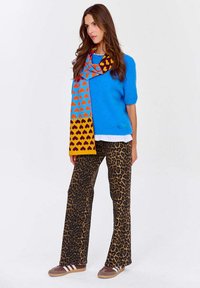 Modrý pletený sveter, farebný šatka s vzorom srdiečok, nohavice so vzorom leopardej kože, hnedé tenisky s bielymi prúžkami, pohodlný strih.