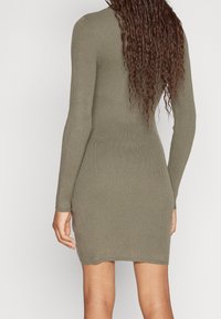 Olivgrön ribbad stickad klänning med långa ärmar, figurnära passform och rund hals, med en längd till mitten av låret och subtil textur.