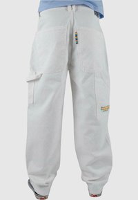 Pantaloni cargo grigi chiari in cotone, con ampie tasche posteriori, tasche laterali e una patch colorata con il logo. Vestibilità rilassata con polsini elasticizzati.