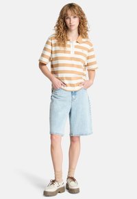 Polo a righe in beige e bianco, in cotone; abbinato a pantaloni corti in denim blu chiaro; scarpe bianche con dettagli marroni.